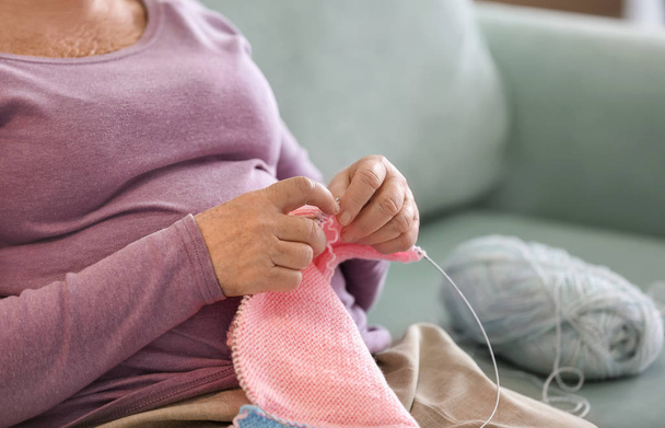 Senior mulher sentada no sofá enquanto tricô suéter em casa
 - Foto, Imagem