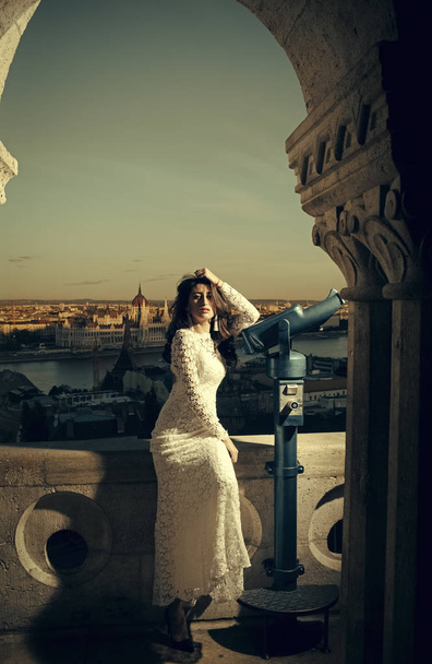 Sexy woman. Woman with telescope at viewpoint on cityscape. Sensual woman with long hair in white wedding dress, fashion. Girl with glamour look and makeup, beauty. Fashion model travel on vacation. - Fotó, kép
