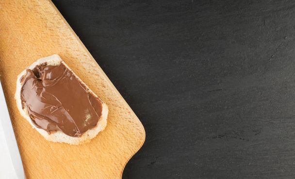 Fatia de baguete com pasta de manteiga de chocolate em fundo de madeira. Creme de cacau na vista superior do sanduíche
 - Foto, Imagem
