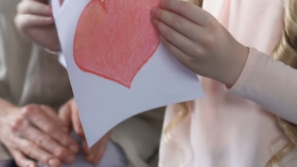 Girl showing grandmother handmade greeting card with heart, family love, care - Materiał filmowy, wideo