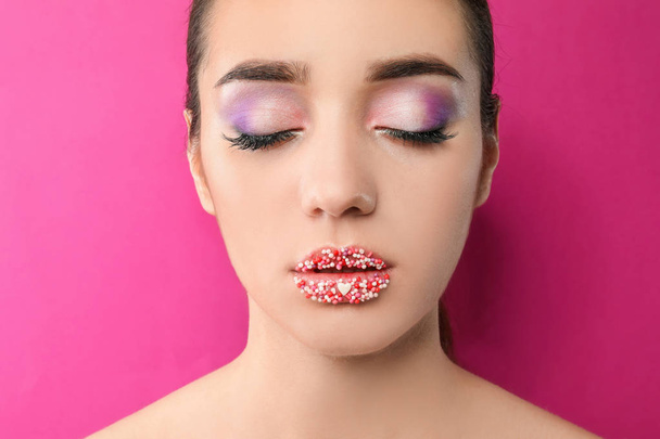 Mooie jonge vrouw met creatieve make-up op kleur achtergrond - Foto, afbeelding