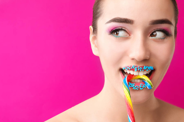 Beautiful young woman with creative makeup and candy cane on color background - Photo, Image