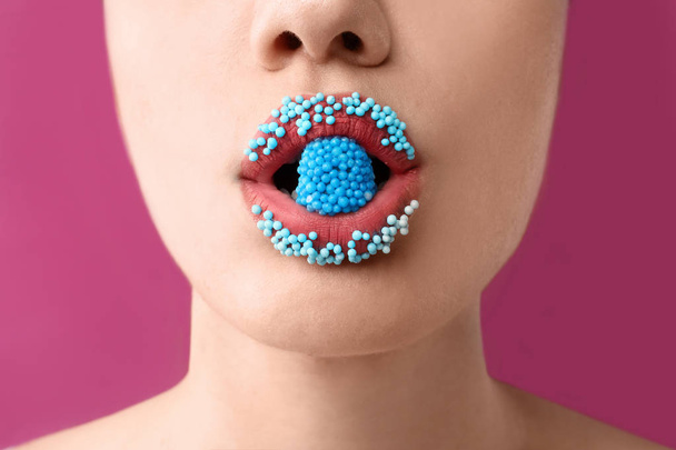 Hermosa mujer joven con maquillaje creativo y dulces en la boca sobre fondo de color, primer plano
 - Foto, imagen