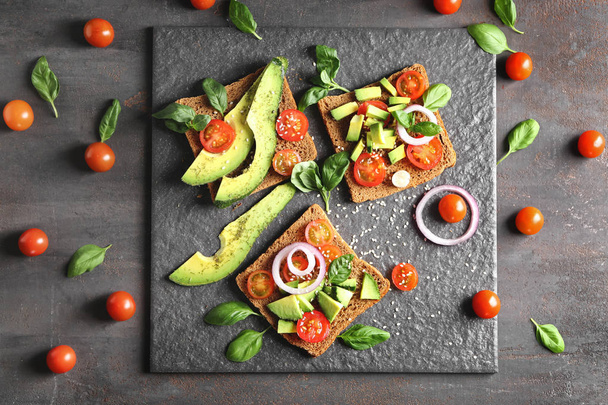 Delicious toasts with avocado on slate plate - Фото, изображение