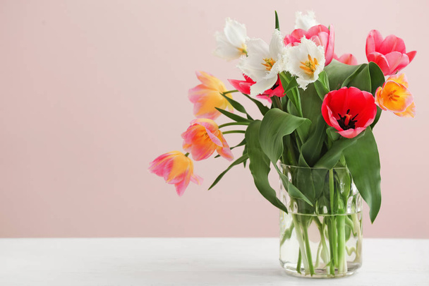 Ваза с красивыми тюльпанами на светлом столе на цветном фоне
 - Фото, изображение