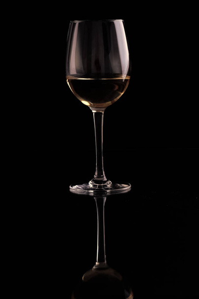 One beautiful clear glass goblet with tasty dry white grape wine reflecting in standing position isolated on black studio background, vertical picture - Фото, зображення
