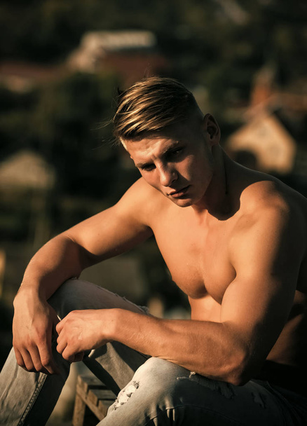 Man face handsome. Man sportsman with muscular torso sit on natural landscape - Фото, изображение