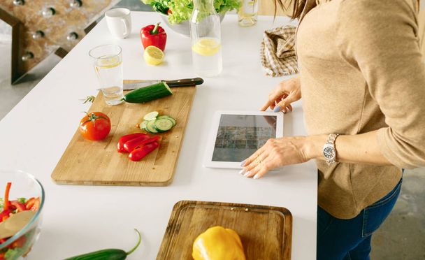 Έννοια της υγιεινής διατροφής. Γυναίκα ψάχνει για χορτοφάγους συνταγή στο διαδίκτυο. Γυναίκα Υγιεινή Χορτοφαγική απλή σαλάτα μαγειρική στο σπίτι στην κουζίνα - Φωτογραφία, εικόνα