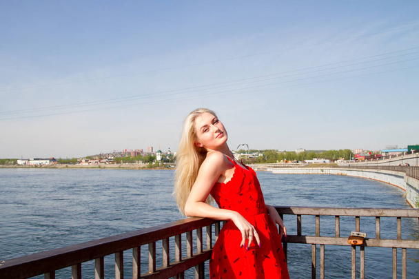 στέκεται κορίτσι σε ένα κόκκινο φόρεμα για το ανάχωμα του ποταμού - Φωτογραφία, εικόνα