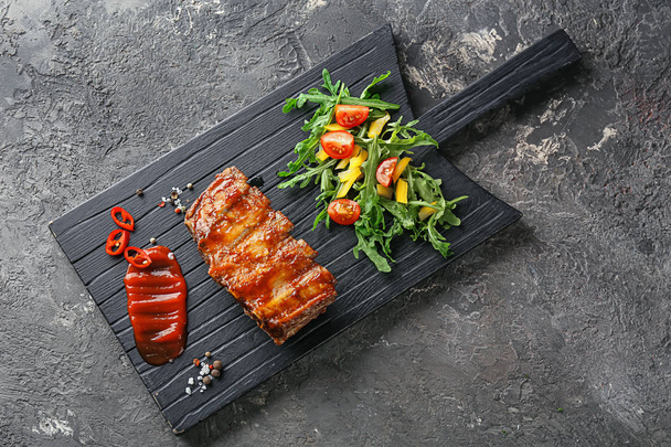 Wooden board with delicious grilled ribs, sauce and vegetable salad - Photo, image