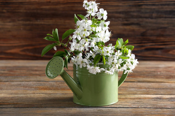 Watering can with beautiful blossoming branches on table - Фото, изображение