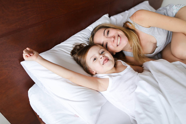陽気な交流においては小さな娘が付いているベッドで横になっている母. - 写真・画像