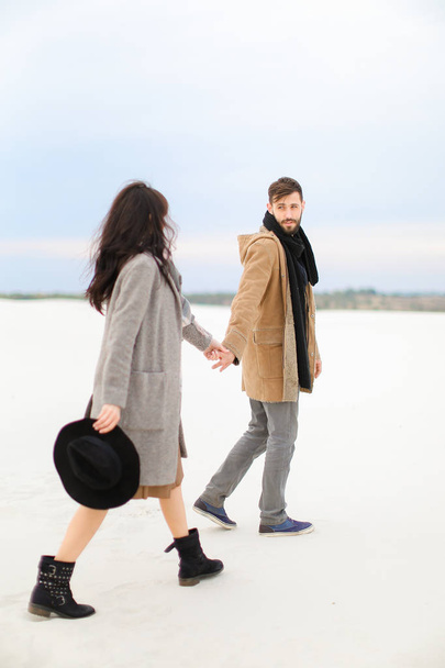 Heureux homme et femme allant sur la neige et tenant la main, portant des manteaux et des écharpes
. - Photo, image