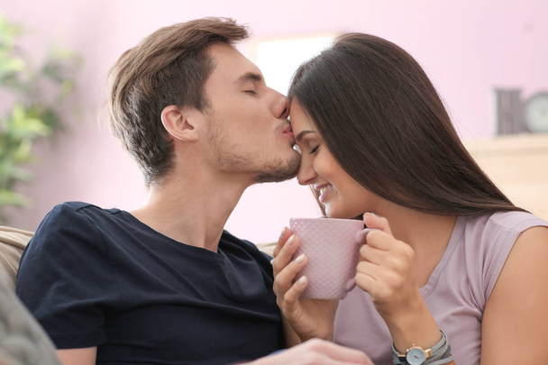 Happy young couple drinking hot coffee while resting at home - Photo, Image