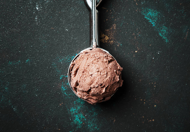 Chocolate ice cream in metal spoon for ice cream, dark background, top view - 写真・画像