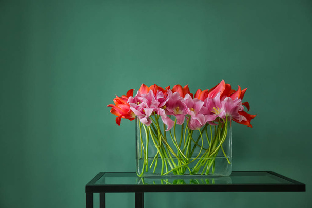 Стеклянная ваза с красивыми тюльпанами на столе на цветном фоне
 - Фото, изображение