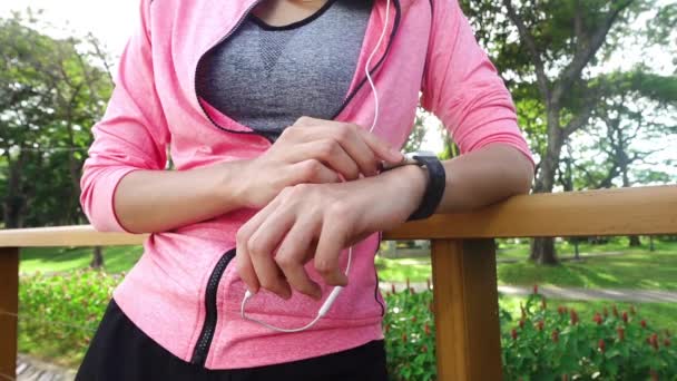 Movimento lento - Mulher bonita asiática em roupas de fitness estão usando um smartwatch para ouvir música, falando ao telefone depois de correr no parque. Atraente jogging feminino saudável
.  - Filmagem, Vídeo