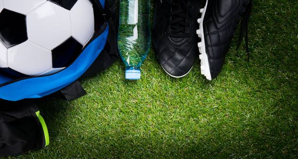 soccer ball, in a sports bag, a bottle of water and black boots, against the background of grass - Photo, image