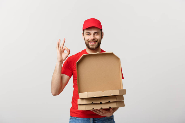 Lieferkonzept: Schöner Pizzabote macht Ok-Schild vor grauem Hintergrund. - Foto, Bild
