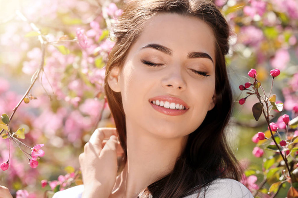 Beautiful young woman near blooming tree in park on spring day - Foto, imagen
