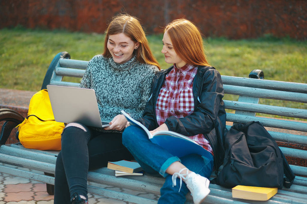 Два студента сидят на скамейке с ноутбуком и книгой
 - Фото, изображение