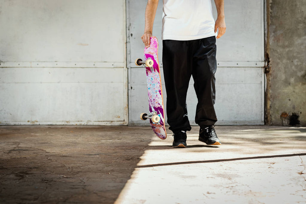 jonge man met een gebruikte skateboard in hand in een concrete skatepark in de zomer - Foto, afbeelding
