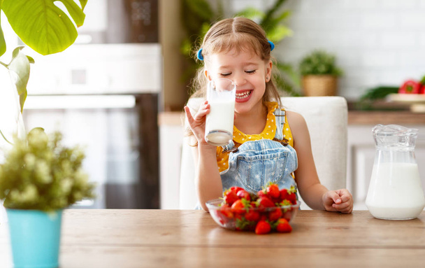 glückliches Baby-Mädchen isst Erdbeeren mit Milch bei hom - Foto, Bild