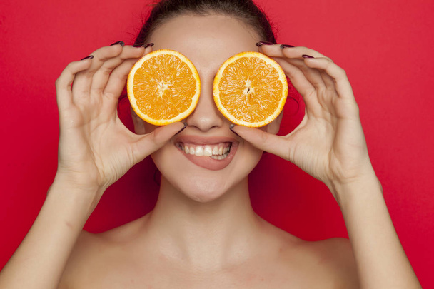Happy young woman posing with slices of orange on her face on a red background - Φωτογραφία, εικόνα
