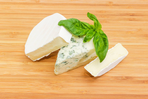 Κομμάτια του μπλε τυρί και τυρί καμαμπέρ τύπου διακοσμημένα με κλαδί πράσινος βασιλικός για το μπαμπού κοπή του σκάφους - Φωτογραφία, εικόνα