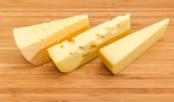 Pezzo di formaggio medio-duro, formaggio di tipo svizzero e formaggio a pasta dura sul tagliere di bambù
 - Foto, immagini