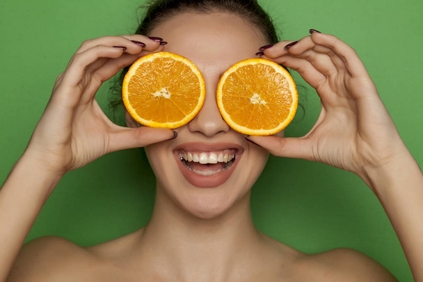 Щаслива молода жінка позує зі скибочками апельсинів на її обличчі на зеленому фоні
 - Фото, зображення