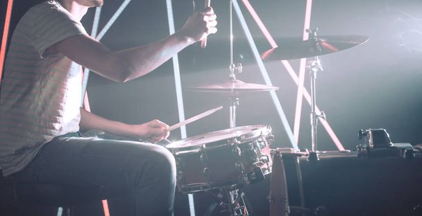 de man speelt de drums, het spel is op de trommel werken met stokken close-up. Op de achtergrond van de gekleurde lampen. Muzikaal concept met een trommel werken. - Foto, afbeelding