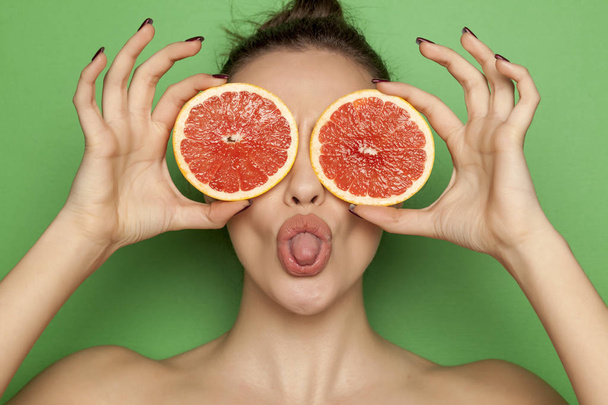 Sexy joven posando con rodajas de pomelo rojo en su cara sobre un fondo verde
 - Foto, Imagen