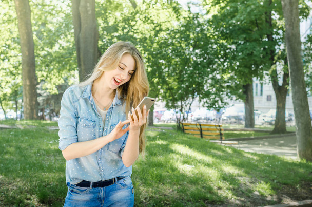 Glimlachend bussines casual vrouw met oproep smartphone mobiele cel met lange haren in de groene natuur park zonnige dag achtergrond - Foto, afbeelding