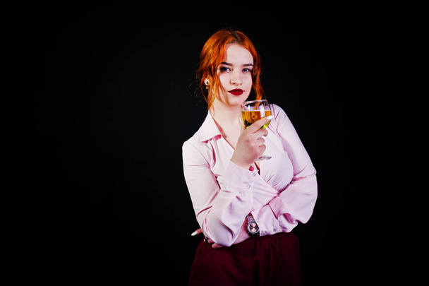 Gorgeous red haired girl in pink blouse and red skirt with glass of wine at hand isolated on black. - Fotoğraf, Görsel