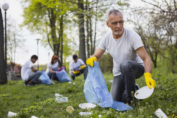 Focused senior volunteer collecting trash - Фото, изображение