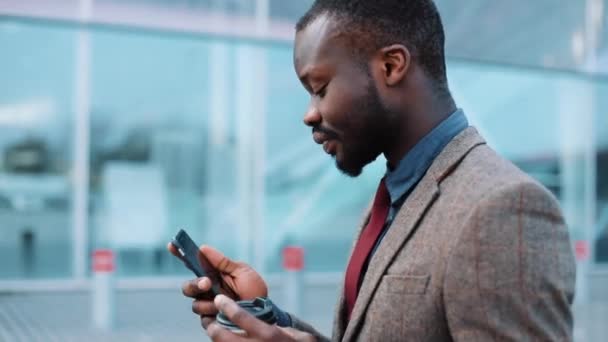 Tired and stressed African American businessman uses a smartphone walking down the street near the office center. The concept of a failed business, bankruptcy, stock upsurge - Filmmaterial, Video