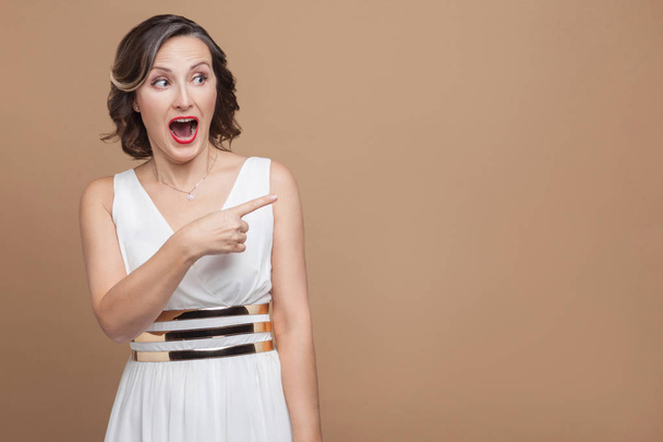 Funny woman pointing finger to right on light brown background, Emotion and feeling concept - Foto, Bild