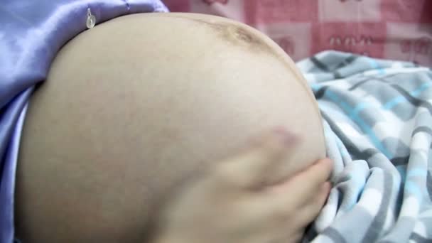 Detailní záběr pohybů dítěte během těhotenství. Těhotná žena leží na posteli a dotýká její nahé velké břicho. Miminko pohybuje uvnitř lůna matky. - Záběry, video