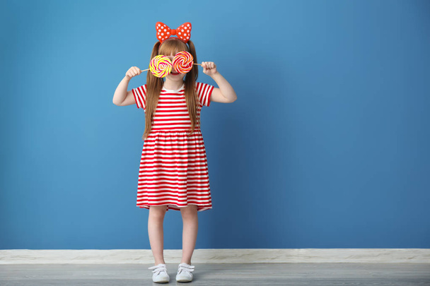 Cute little girl with lollipops near color wall - Fotó, kép