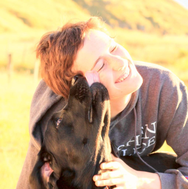 Černý Labrador pes líbání tvář mladé ženy, která se usmívá úplně s radosti v jasné ranní slunce - Fotografie, Obrázek
