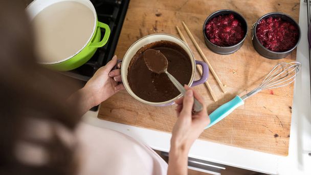 Mujer haciendo desierto de chocolate con frambuesas en su cocina vista por encima del hombro desde arriba
. - Foto, Imagen