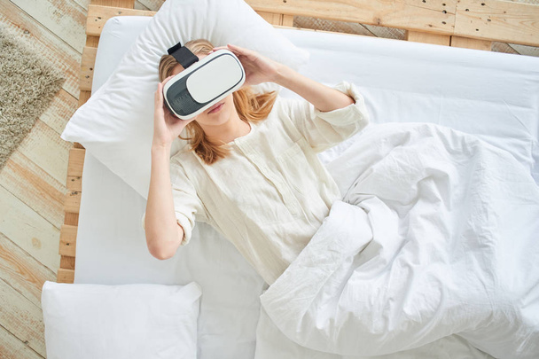 woman using VR-glasses and enjoying while lying on bed at home  - Fotografie, Obrázek