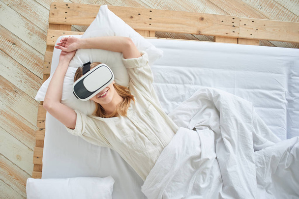 woman using VR-glasses and enjoying while lying on bed at home  - Foto, afbeelding