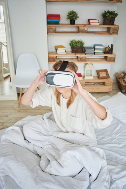 woman in VR-glasses enjoying while sitting on bed at home  - Photo, image