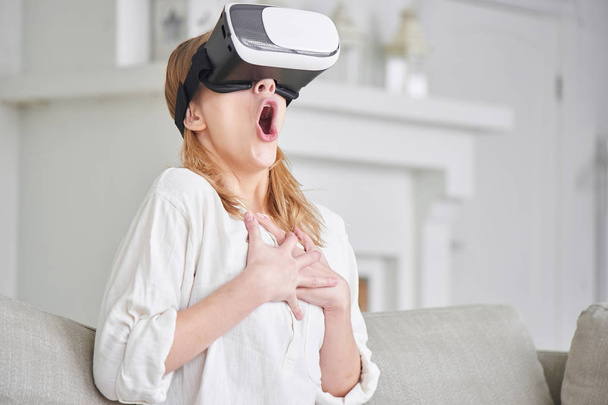 woman in VR-glasses enjoying while sitting on sofa at home  - Φωτογραφία, εικόνα