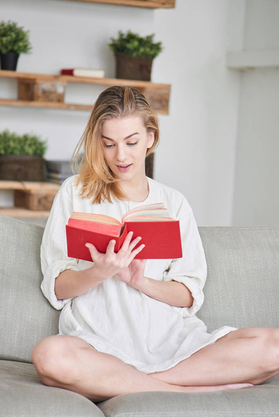 woman sitting on sofa and reading red book at home  - Foto, afbeelding