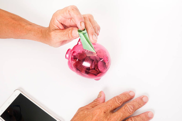Asian senior inserting notes into a red piggy bank. Saving, retirement plan, retirees financial planning concept - Photo, image