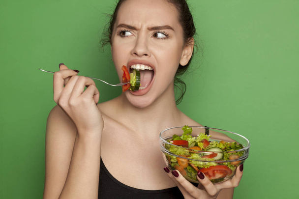 Young beautiful woman eating salad on a green background - Photo, Image