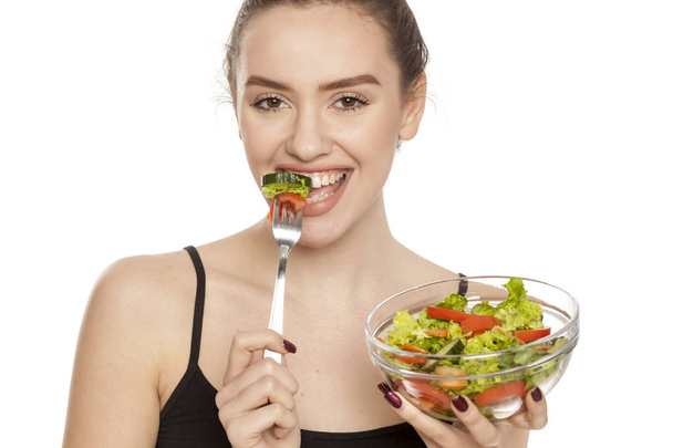Νεαρή όμορφη γυναίκα τρώει σαλάτα σε λευκό φόντο - Φωτογραφία, εικόνα